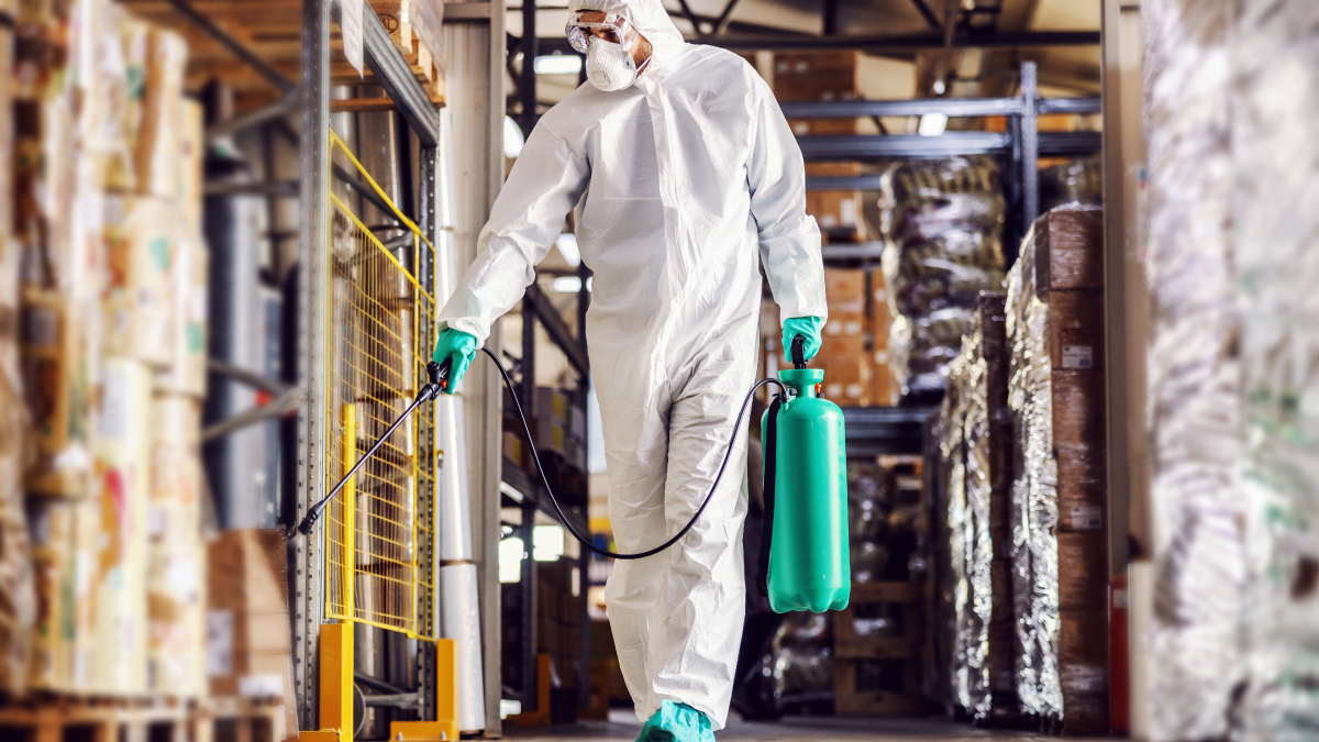 Man in protective suit and mask disinfects warehouse full of food products