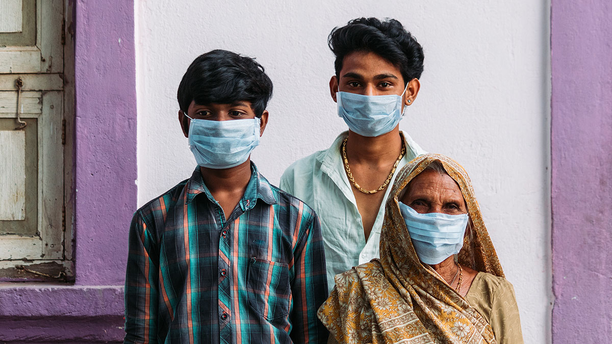 Indian family with masks on stand against purple wall