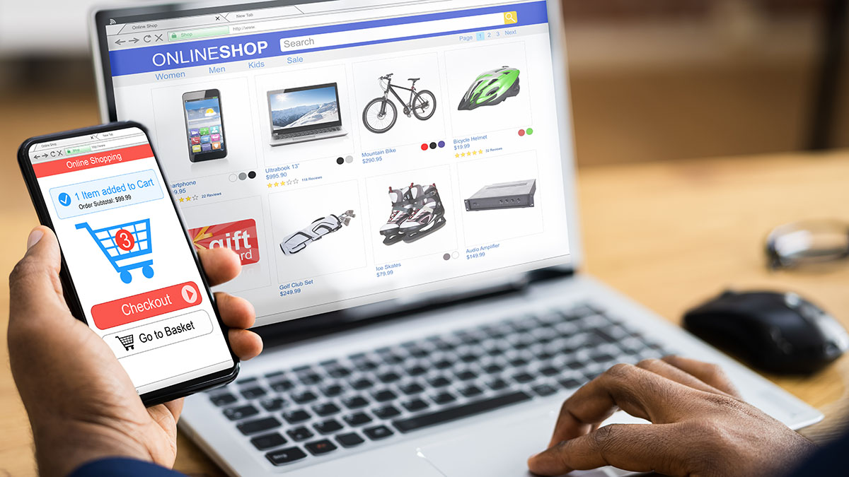 Man online shopping at computer with cellphone in hand