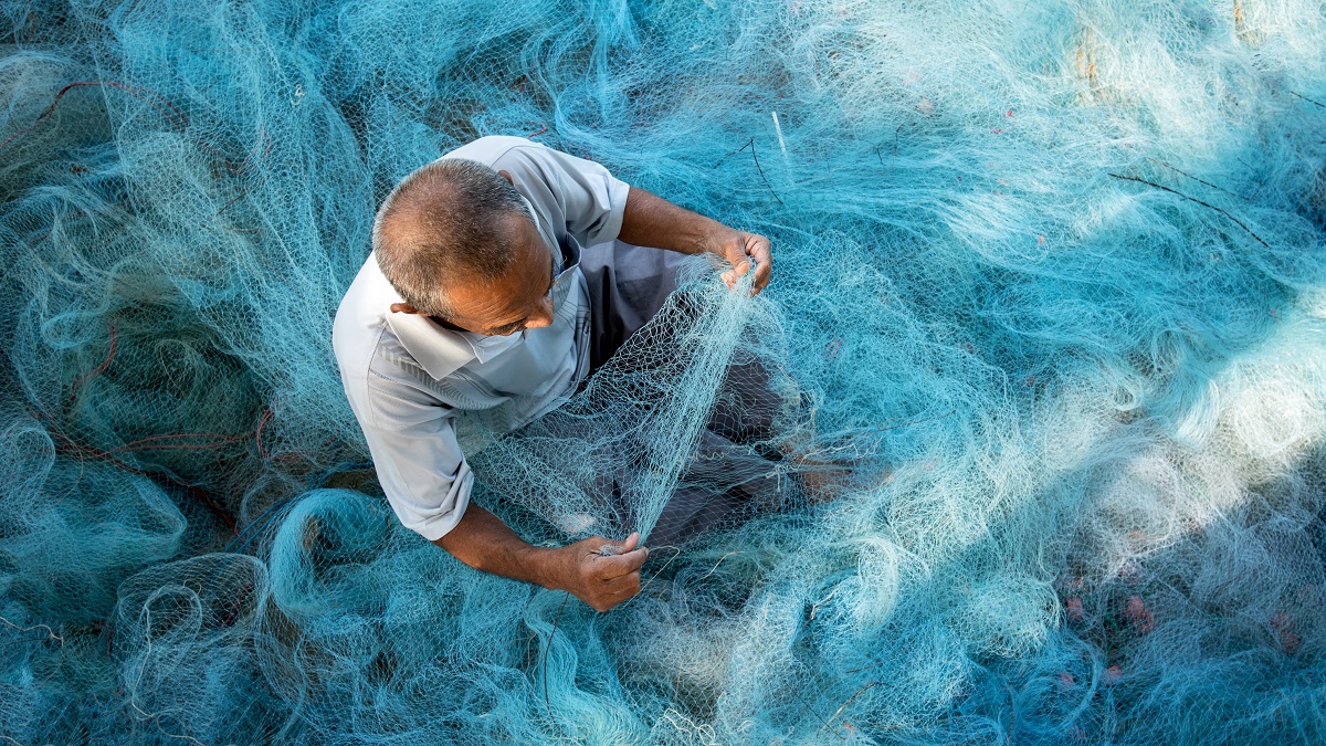 Man fixes blue fishing nets in Thailand
