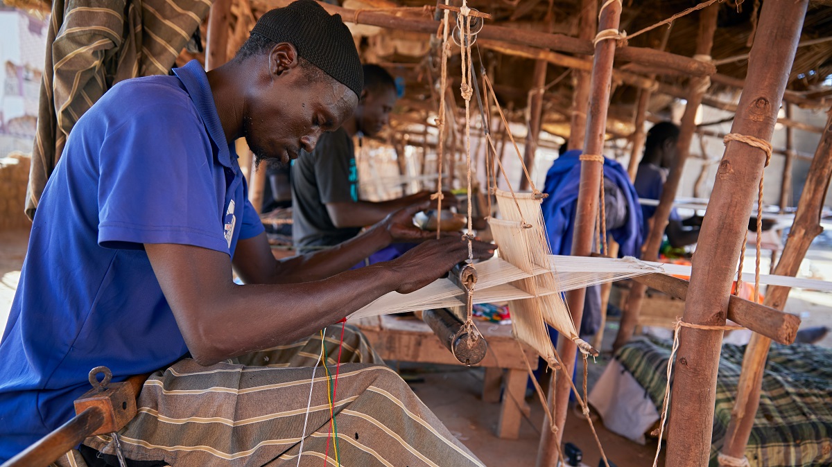 Mopti, Mali. A weaver working at outdoor street carpet and textile weaving factory.