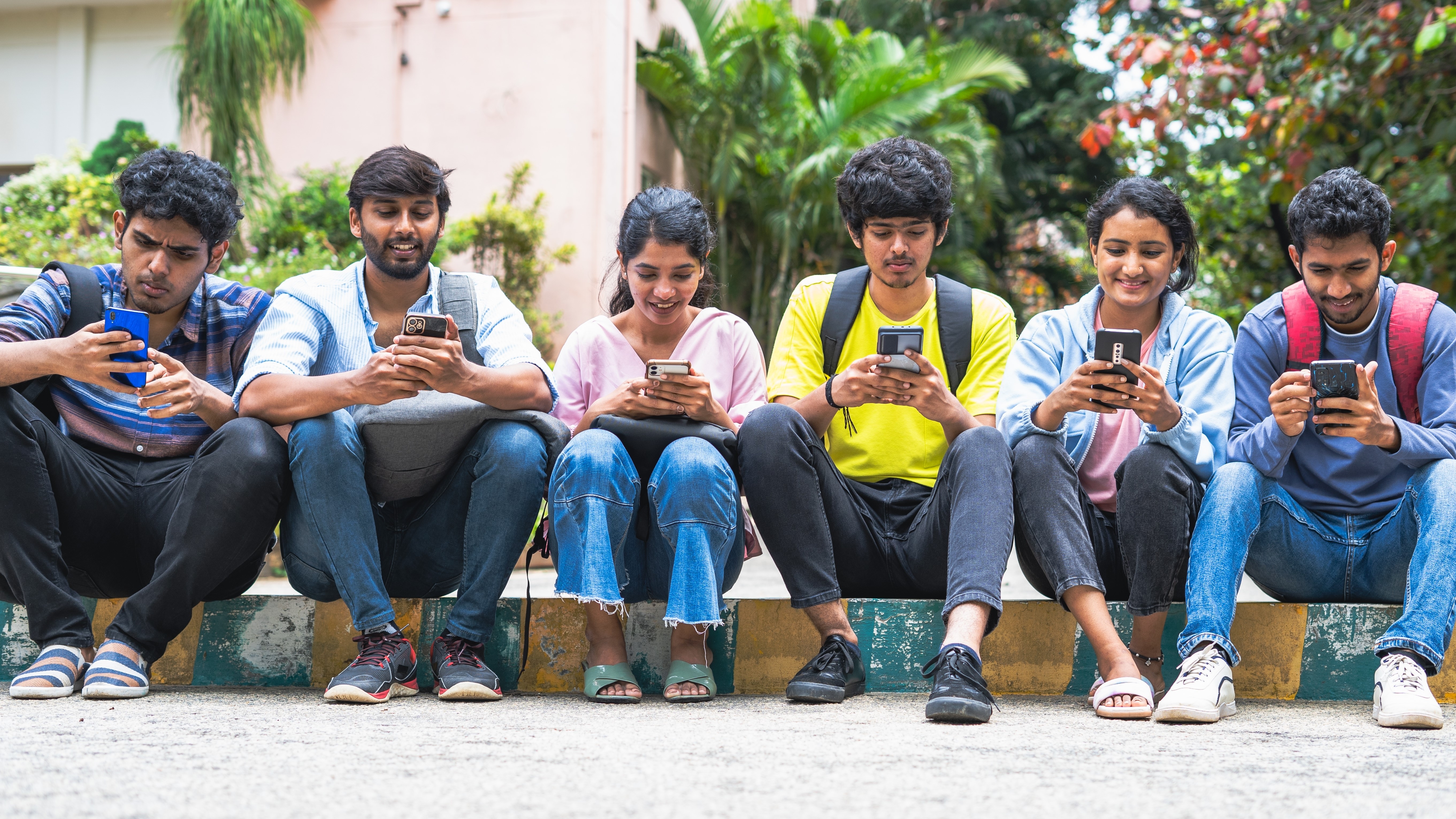 Group of indian college students busy using mobile phone at campus