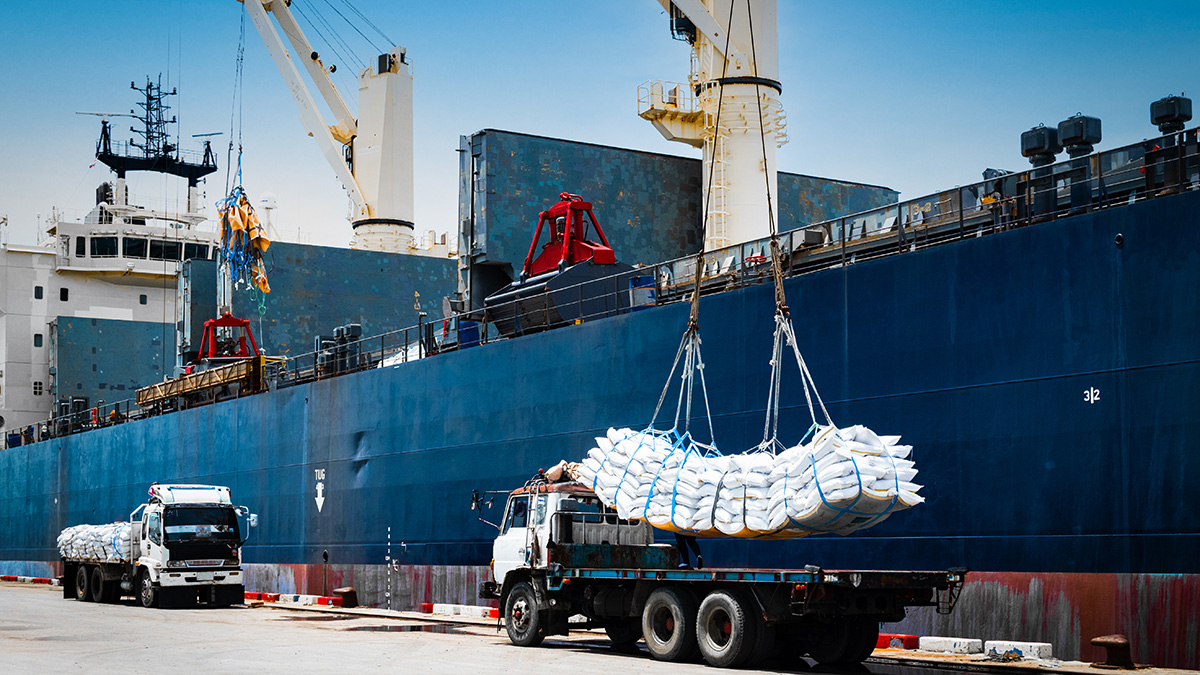 Ship crane lifting cargo from truck to ship for export.