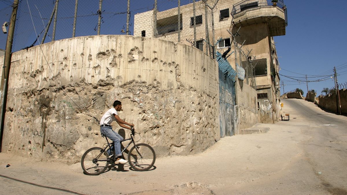 A young resident bikes past a bulletpocked wall of UNRWA's School for Girls