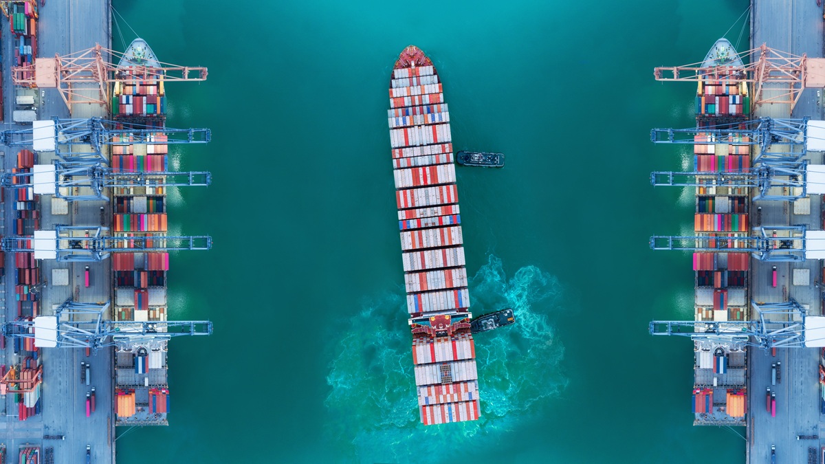 Container ship moving past seaport warehouse.