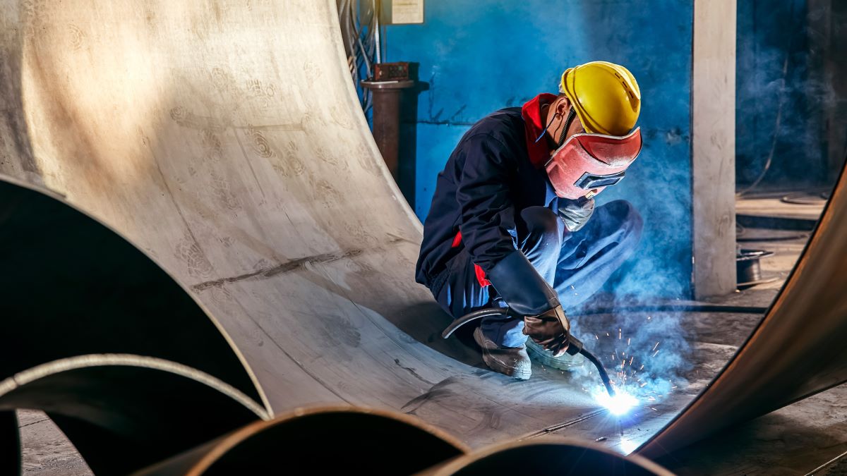 Worker welding industrial steel components in a manufacturing facility.