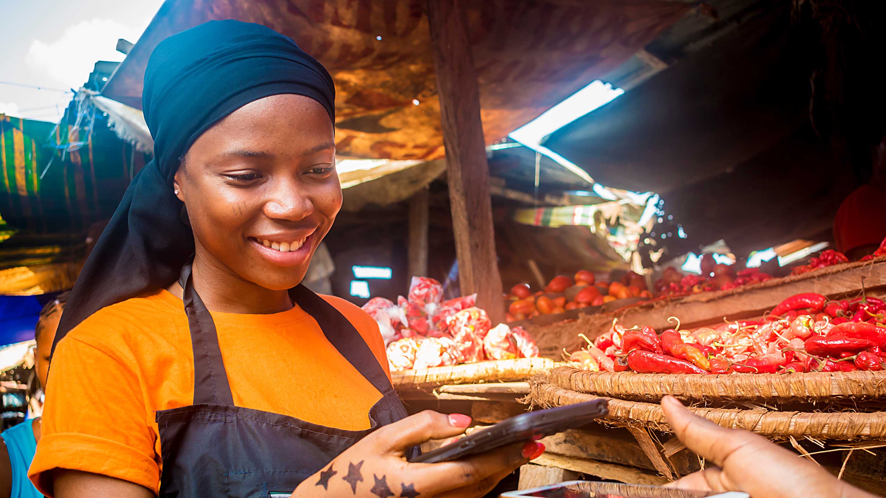 young african woman selling tomatoes in a local african market receiving payment via mobile phone transfer