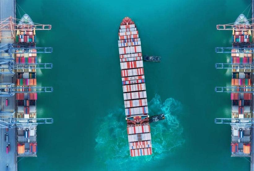 Container ship moving past seaport warehouse.