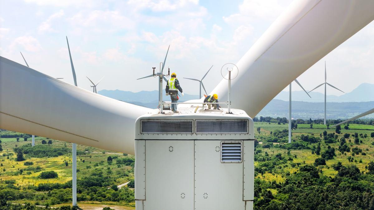 Expert team maintaining and inspecting wind turbines efficient clean energy production. surrounded by vast green fields and distant mountains, with multiple turbines spinning under partly cloudy sky.