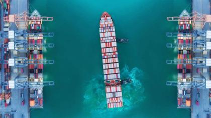 Container ship moving past seaport warehouse.