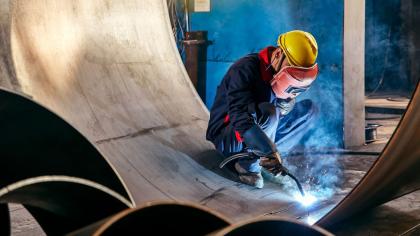 Worker welding industrial steel components in a manufacturing facility.