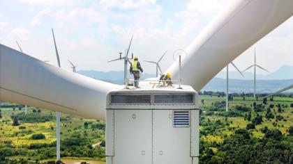 Expert team maintaining and inspecting wind turbines efficient clean energy production. surrounded by vast green fields and distant mountains, with multiple turbines spinning under partly cloudy sky.